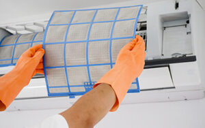 ¿Por qué es importante limpiar el aire acondicionado regularmente? Manos de una persona limpiando los filtros del aire acondicionado